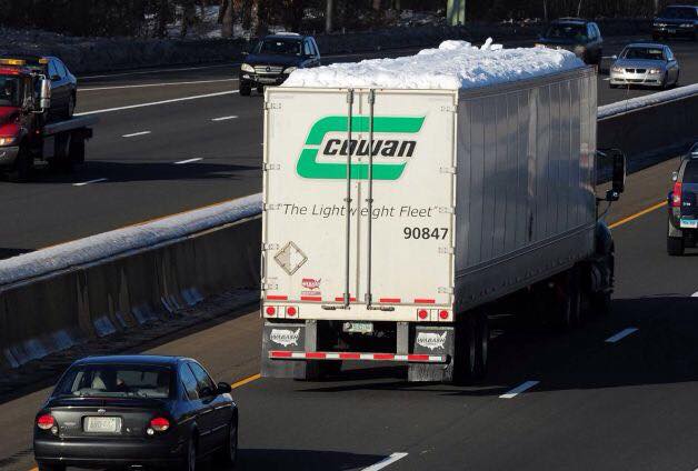 Tractor-trailer driving on a highway with snow piled on its roof
